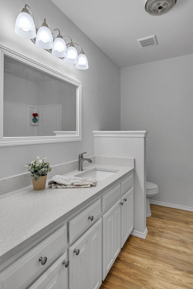 bathroom featuring baseboards, visible vents, toilet, wood finished floors, and vanity