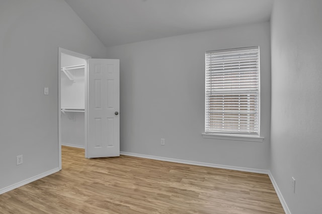 unfurnished bedroom featuring lofted ceiling, light wood-style flooring, baseboards, a spacious closet, and a closet