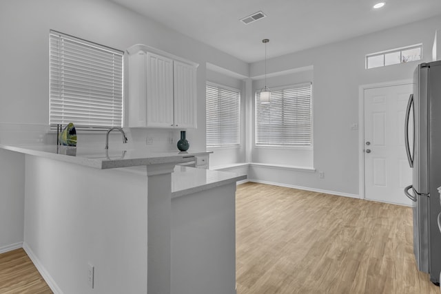 kitchen featuring decorative light fixtures, visible vents, freestanding refrigerator, white cabinetry, and a peninsula