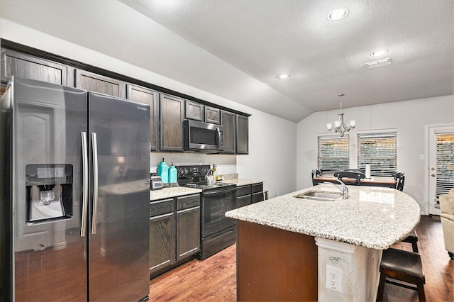 kitchen featuring stainless steel appliances, a notable chandelier, pendant lighting, vaulted ceiling, and a center island with sink