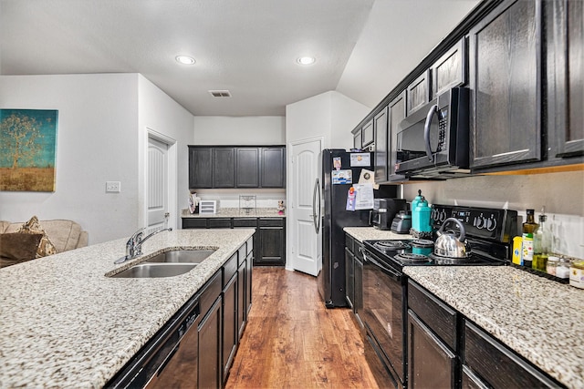 kitchen featuring light stone countertops, sink, black appliances, hardwood / wood-style flooring, and lofted ceiling