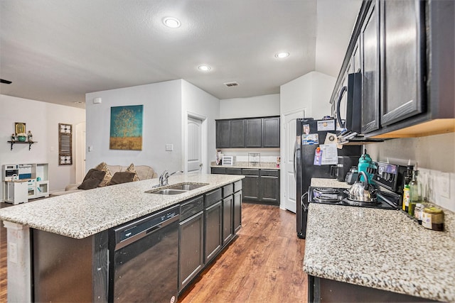 kitchen with sink, light stone counters, wood-type flooring, a center island with sink, and black appliances