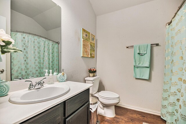 bathroom featuring vanity, wood-type flooring, lofted ceiling, and toilet