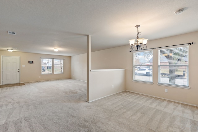 carpeted spare room with a textured ceiling and an inviting chandelier