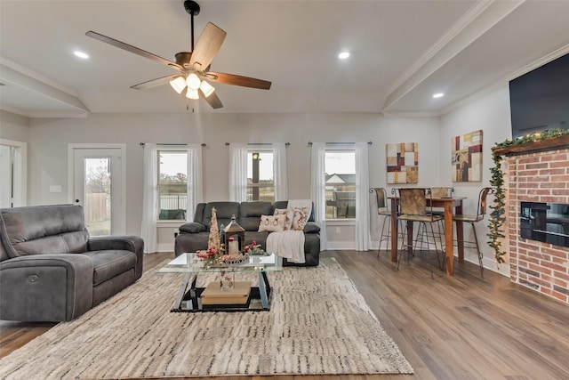 living room with hardwood / wood-style flooring, ceiling fan, ornamental molding, and a fireplace