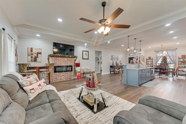 living room featuring ceiling fan with notable chandelier, light wood-type flooring, crown molding, and a brick fireplace