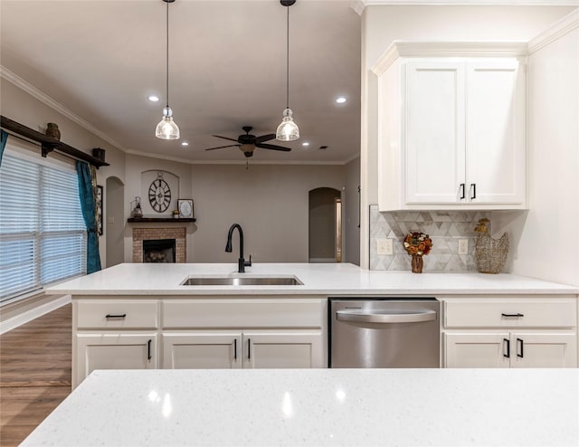 kitchen featuring dishwasher, sink, a brick fireplace, ceiling fan, and white cabinetry