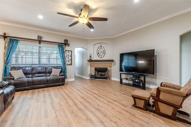 living room with a brick fireplace, light hardwood / wood-style flooring, ceiling fan, and ornamental molding