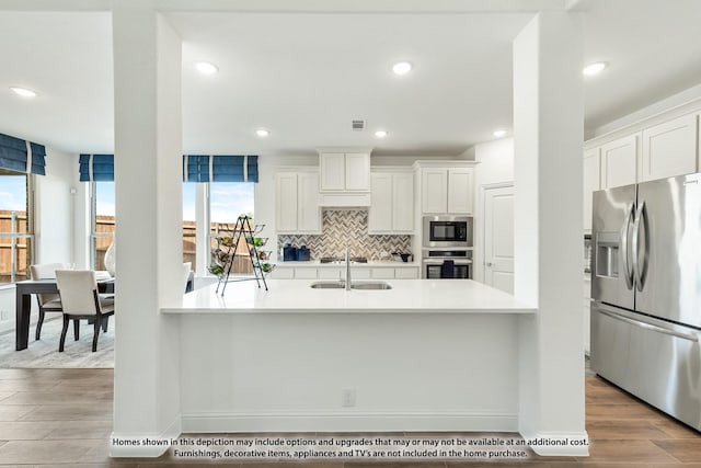 kitchen with sink, decorative backsplash, appliances with stainless steel finishes, light hardwood / wood-style floors, and white cabinetry