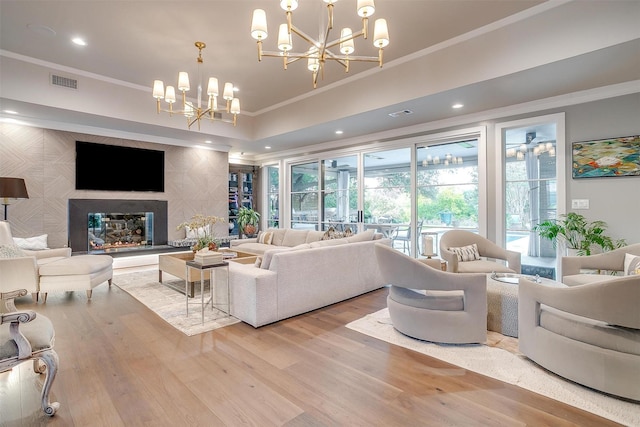 living room with an inviting chandelier, a fireplace, ornamental molding, and light hardwood / wood-style floors