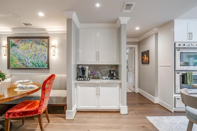 kitchen with tasteful backsplash, ornamental molding, white cabinets, stainless steel double oven, and light wood-type flooring