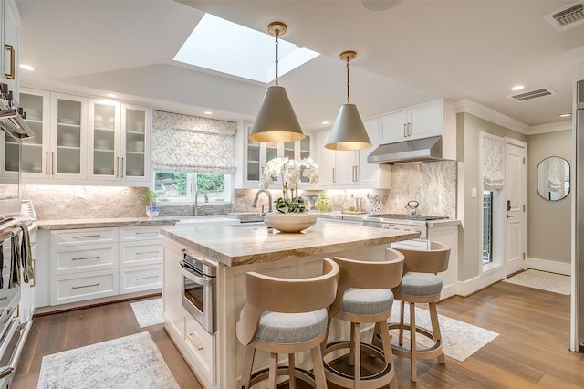 kitchen with dark wood-type flooring, hanging light fixtures, light stone countertops, white cabinets, and a center island with sink