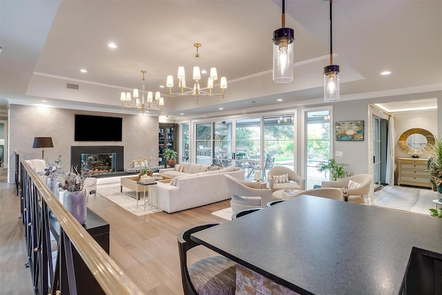 living room featuring ornamental molding, a tray ceiling, light hardwood / wood-style floors, and a notable chandelier