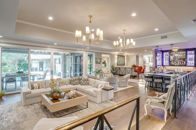 living room with sink, a chandelier, ornamental molding, a raised ceiling, and light wood-type flooring