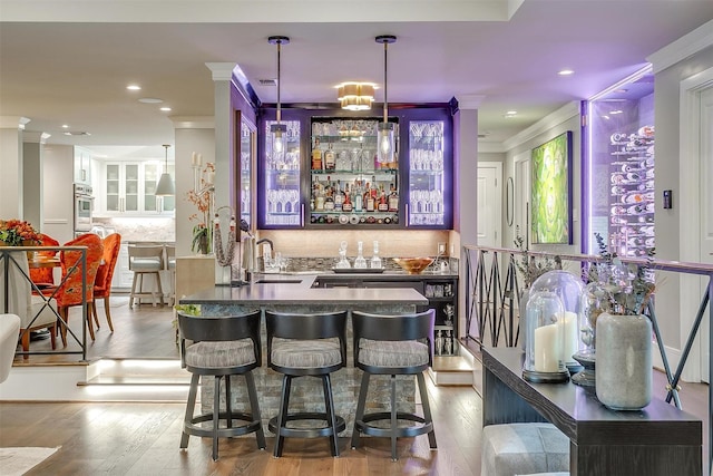 bar with sink, crown molding, tasteful backsplash, light wood-type flooring, and pendant lighting