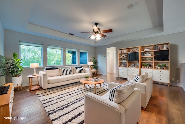 living room featuring hardwood / wood-style floors, a tray ceiling, and ceiling fan