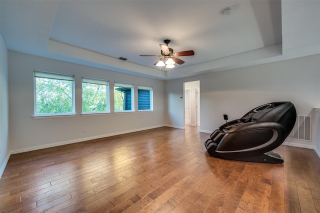 living area with a raised ceiling, ceiling fan, and wood-type flooring