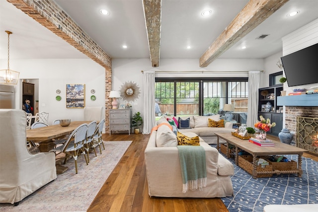 living room featuring dark wood-type flooring, a notable chandelier, a fireplace, and beamed ceiling