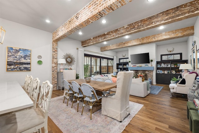 dining area featuring beamed ceiling, hardwood / wood-style floors, and a brick fireplace