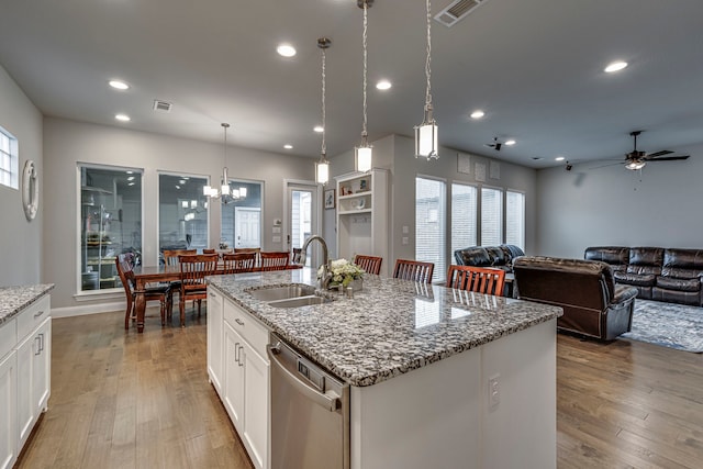 kitchen featuring white cabinets, dishwasher, light stone counters, and an island with sink