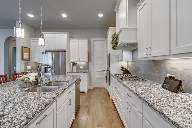 kitchen with sink, light hardwood / wood-style flooring, decorative light fixtures, white cabinets, and appliances with stainless steel finishes