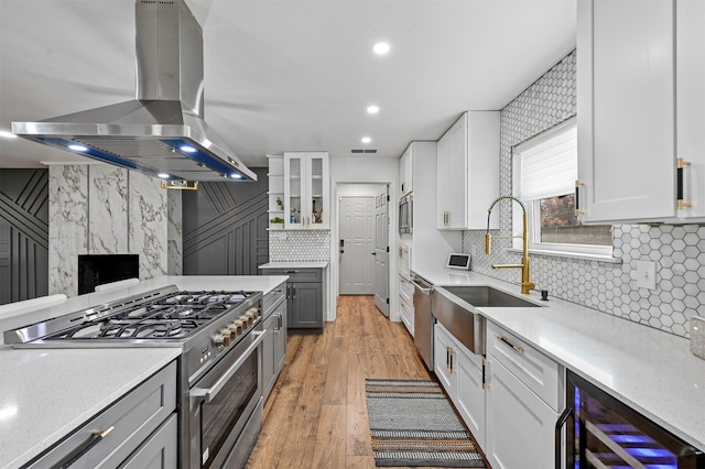 kitchen featuring appliances with stainless steel finishes, ventilation hood, beverage cooler, light hardwood / wood-style flooring, and white cabinets