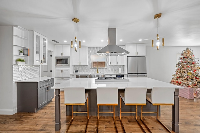 kitchen with island exhaust hood, light wood-type flooring, stainless steel appliances, and white cabinets