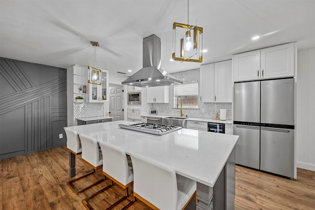 kitchen featuring island exhaust hood, appliances with stainless steel finishes, light hardwood / wood-style flooring, and hanging light fixtures