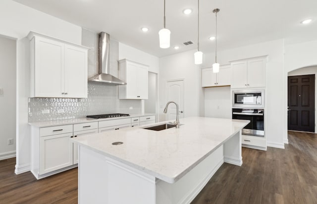 kitchen with wall chimney range hood, oven, sink, built in microwave, and an island with sink