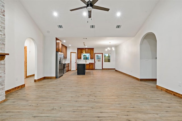 unfurnished living room featuring ceiling fan with notable chandelier, a fireplace, a high ceiling, and light hardwood / wood-style flooring