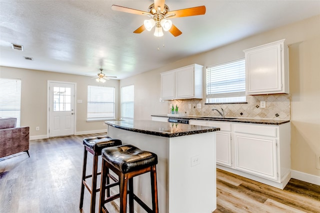 kitchen with ceiling fan, a kitchen island, tasteful backsplash, light hardwood / wood-style floors, and white cabinets