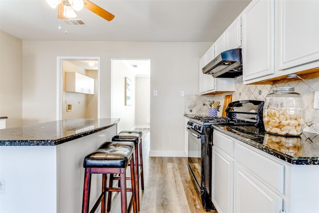 kitchen with light wood-type flooring, backsplash, white cabinets, black gas range, and a center island