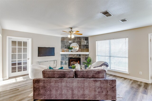 living room featuring a tile fireplace, a textured ceiling, light hardwood / wood-style flooring, and ceiling fan