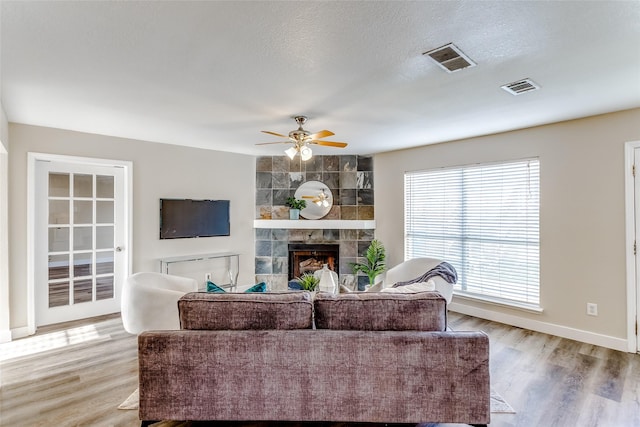 living room featuring ceiling fan, a tile fireplace, light hardwood / wood-style floors, and a textured ceiling