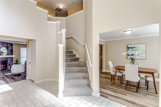 stairs featuring hardwood / wood-style floors, ornamental molding, a fireplace, and a high ceiling