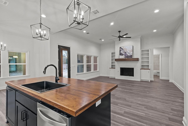 kitchen with a fireplace, wood counters, decorative light fixtures, sink, and a center island with sink