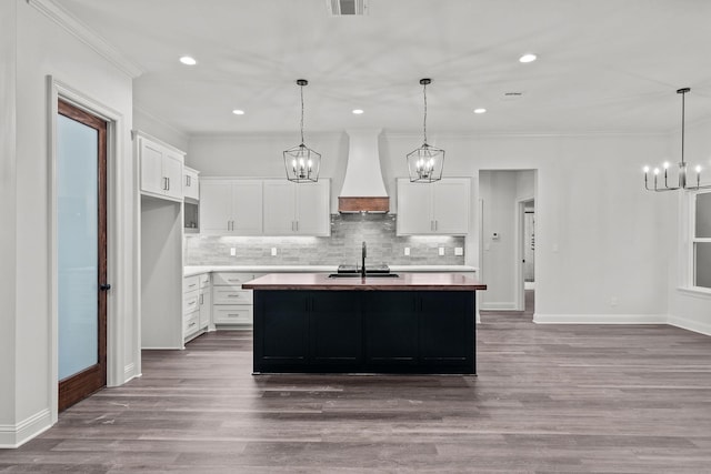 kitchen with premium range hood, white cabinetry, a chandelier, and a center island with sink