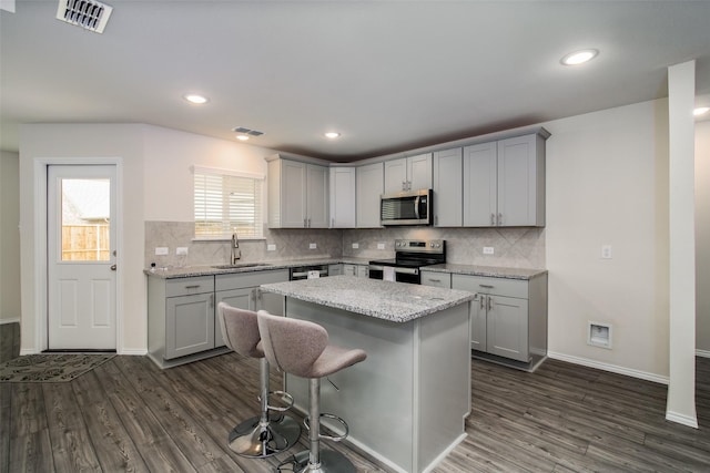 kitchen with a kitchen breakfast bar, sink, light stone countertops, appliances with stainless steel finishes, and a kitchen island