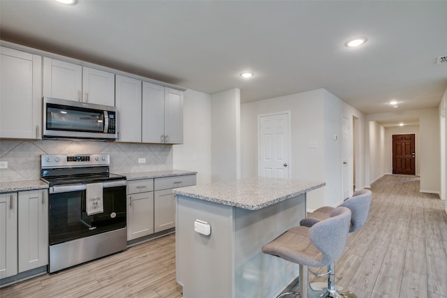 kitchen featuring stainless steel appliances, backsplash, light hardwood / wood-style floors, a kitchen bar, and a kitchen island