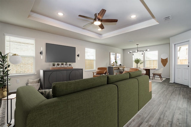 living room with ceiling fan with notable chandelier, light hardwood / wood-style floors, a raised ceiling, and crown molding