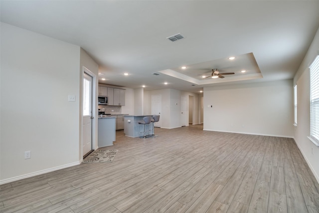 unfurnished living room with ceiling fan, light hardwood / wood-style floors, and a raised ceiling