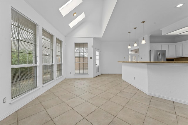 interior space featuring white cabinetry, light tile patterned floors, stainless steel fridge, pendant lighting, and vaulted ceiling with skylight