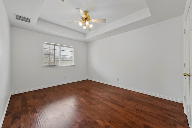 empty room with dark wood-type flooring, ceiling fan, and a tray ceiling