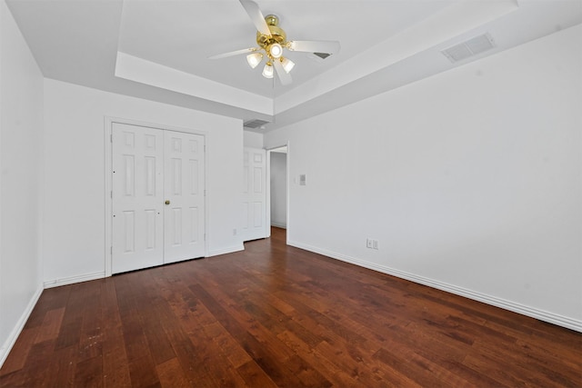 unfurnished bedroom with a raised ceiling, dark hardwood / wood-style floors, ceiling fan, and a closet