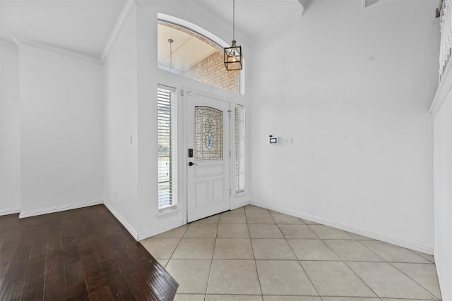 foyer entrance with an inviting chandelier, ornamental molding, a high ceiling, and light tile patterned floors