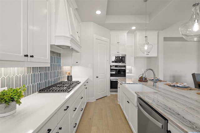 kitchen with a sink, appliances with stainless steel finishes, custom range hood, white cabinets, and light wood-style floors