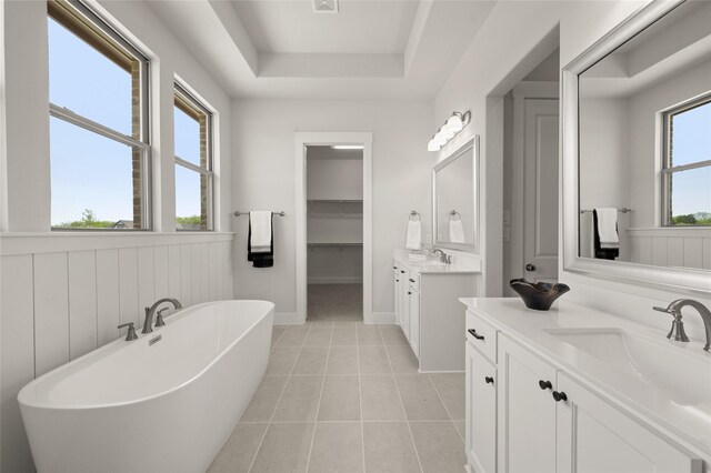 bathroom featuring a freestanding tub, a tray ceiling, tile patterned floors, a sink, and two vanities