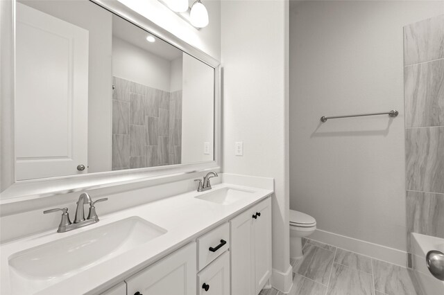 bathroom with baseboards, toilet, double vanity, and a sink