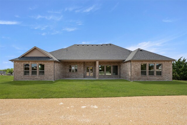 rear view of property featuring a patio, brick siding, a shingled roof, and a lawn