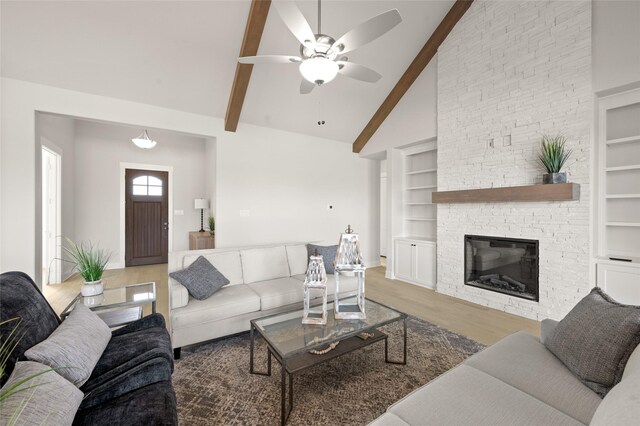 living room with beamed ceiling, a fireplace, built in shelves, wood finished floors, and a ceiling fan